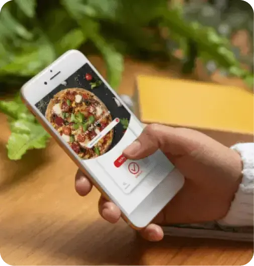 Personne qui parcourt un catalogue de produits alimentaires sur un téléphone mobile, avec des ingrédients frais en arrière-plan
